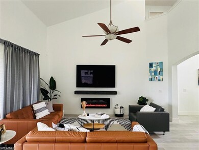 Living room with high vaulted ceiling, arched walkways, a warm lit fireplace, light wood-type flooring, and a ceiling fan