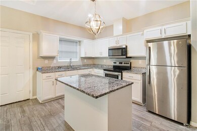 Kitchen featuring white cabinetry, light stone counters, appliances with stainless steel finishes, a kitchen island, and light wood-type flooring