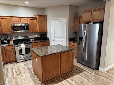 Kitchen featuring stainless steel appliances, brown cabinetry, light wood-type flooring, dark stone countertops, and a kitchen island