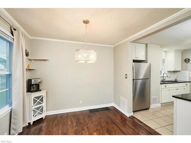 Kitchen featuring a textured ceiling, ornamental molding, stainless steel refrigerator, backsplash, white cabinetry, and light tile floors