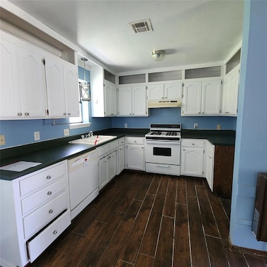 Kitchen featuring white appliances, under cabinet range hood, dark countertops, and dark wood-style floors