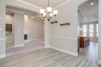 Spare room with a notable chandelier, light wood-type flooring, beamed ceiling, crown molding, and coffered ceiling