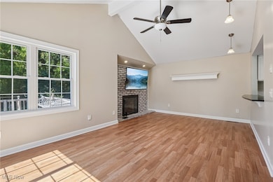 Unfurnished living room featuring high vaulted ceiling, light wood-style floors, a ceiling fan, beamed ceiling, and a brick fireplace