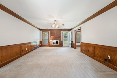 Unfurnished living room with a wainscoted wall, crown molding, light colored carpet, ceiling fan, and a fireplace