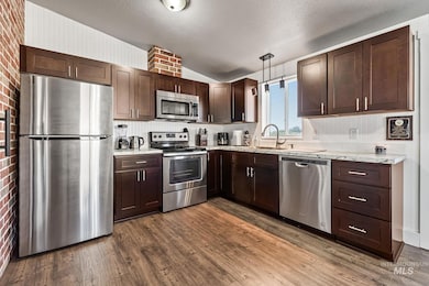 Kitchen with appliances with stainless steel finishes, lofted ceiling, dark brown cabinetry, dark wood-type flooring, and light stone countertops