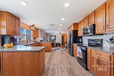 Kitchen featuring stainless steel appliances, a peninsula, light wood finished floors, decorative backsplash, and brown cabinetry