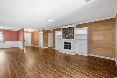 Unfurnished living room featuring ornamental molding, a fireplace with raised hearth, dark wood-style floors, and wood walls