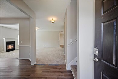 Carpeted entrance foyer with wood finished floors, a glass covered fireplace, baseboards, and stairway