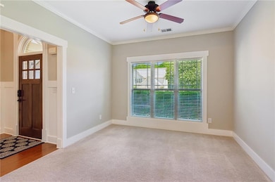 Foyer entrance featuring ornamental molding, carpet, and a ceiling fan