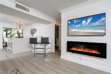 Living room featuring ornamental molding, a warm lit fireplace, wood finished floors, and a chandelier