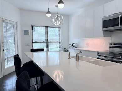 Kitchen with a kitchen bar, stainless steel appliances, hanging light fixtures, and white cabinetry