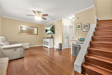 Living area with stairway, wood finished floors, ceiling fan, crown molding, and baseboards