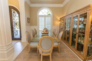 Dining area with crown molding, decorative columns, light tile patterned floors, and wainscoting
