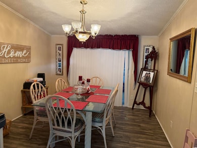 Dining room with dark wood-style floors, a chandelier, crown molding, and a textured ceiling