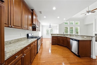 Kitchen featuring appliances with stainless steel finishes, a sink, light wood-type flooring, under cabinet range hood, and a ceiling fan