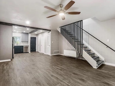 Unfurnished living room with dark wood finished floors, beamed ceiling, ceiling fan, and stairway