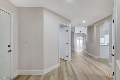 Hall with arched walkways, baseboards, light wood-