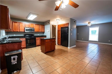 Kitchen with black appliances, ceiling fan, dark countertops, and light tile patterned floors