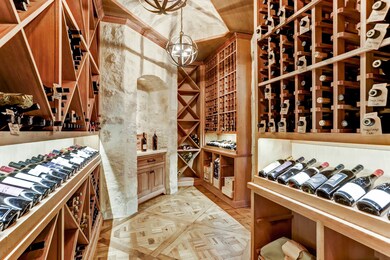 1000+ bottle temperature controlled wine room with iron orb chandeliers and stone walls located efficiently next to the dining room and butler's pantry.  Note patterned wood floors and display lighting.