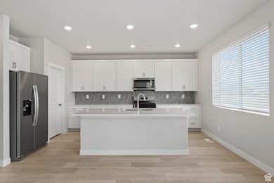 Kitchen featuring a sink, light countertops, an island with sink, stainless steel appliances, and decorative backsplash