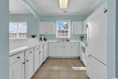 Kitchen with white appliances, a textured ceiling, white cabinets, light countertops, and light tile patterned flooring