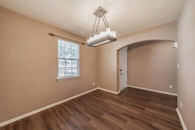 Empty room with arched walkways, dark wood-style flooring, and a chandelier