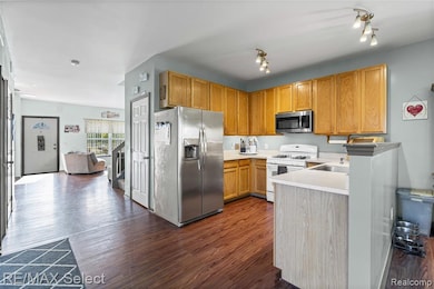 Kitchen featuring appliances with stainless steel finishes, dark wood-style floors, light countertops, brown cabinetry, and a peninsula