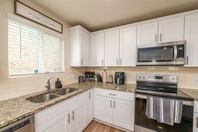 Kitchen featuring decorative backsplash, light hardwood / wood-style flooring, white cabinets, and stainless steel appliances