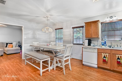 Kitchen featuring light countertops, dishwasher, brown cabinets, light wood-style flooring, and decorative light fixtures