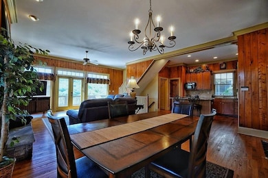 Dining room featuring ornamental molding, wooden walls, dark wood finished floors, a ceiling fan, and a chandelier