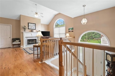 Stairs with healthy amount of natural light, wood finished floors, vaulted ceiling, ceiling fan, and a premium fireplace