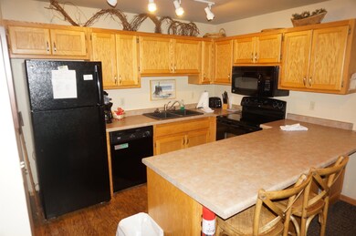 Kitchen featuring a breakfast bar, black appliances, a peninsula, light countertops, and dark wood-style flooring