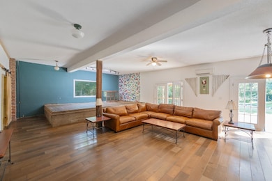 Living room with wood-type flooring, beamed ceiling, a wall unit AC, and a ceiling fan