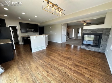Kitchen with appliances with stainless steel finishes, dark cabinets, dark wood-type flooring, a center island with sink, and open floor plan