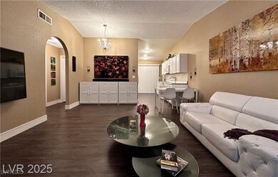 Living room with arched walkways, a chandelier, dark wood finished floors, lofted ceiling, and a textured ceiling