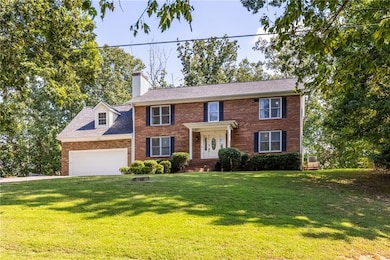 Colonial inspired home featuring a front lawn, brick siding, a chimney, and driveway
