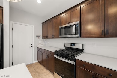 Kitchen with stainless steel appliances, light tile patterned floors, dark brown cabinets, recessed lighting, and decorative backsplash