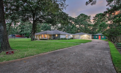 This charming home features a spacious front yard with mature trees, providing plenty of shade and privacy. It has a welcoming front porch, a long driveway leading to a two-car garage, and a separate storage building, ideal for additional storage or a workshop. The property is set in a lush, green environment, offering a serene and inviting atmosphere.
