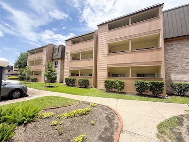 This photo shows a three-story apartment building with covered balconies, surrounded by well-maintained landscaping and a pathway. The exterior features a mix of brick and wood siding, giving it a modern look.