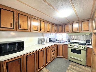 Kitchen featuring range with gas cooktop, light countertops, black microwave, brown cabinets, and a textured ceiling