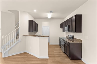 Kitchen with appliances with stainless steel finishes, dark stone countertops, light wood finished floors, dark brown cabinetry, and recessed lighting