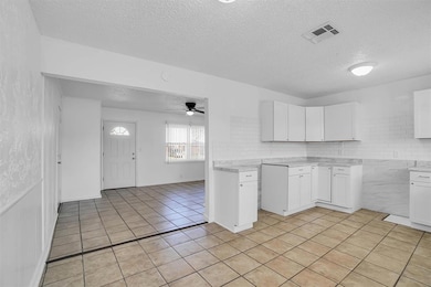 Kitchen with a textured ceiling, light tile patterned flooring, light countertops, ceiling fan, and white cabinetry