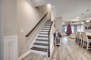 Stairs with wood finished floors, crown molding, and ceiling fan