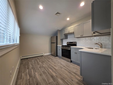 Kitchen with gray cabinets, stainless steel appliances, backsplash, baseboard heating, and vaulted ceiling