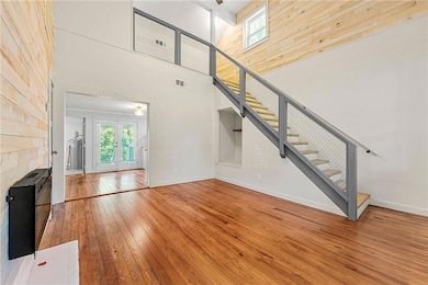 Unfurnished living room with wood-type flooring, plenty of natural light, wood walls, french doors, and stairs