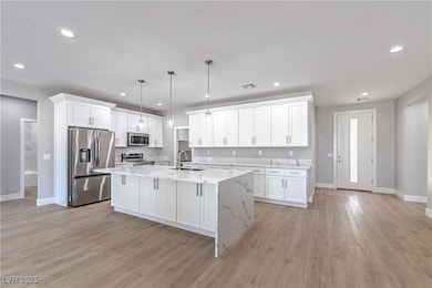 Kitchen featuring stainless steel appliances, white cabinets, light stone counters, hanging light fixtures, and recessed lighting