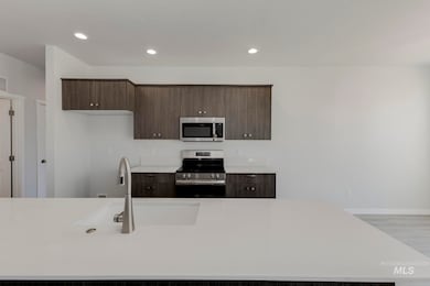 Kitchen featuring dark brown cabinetry, appliances with stainless steel finishes, modern cabinets, recessed lighting, and light stone countertops