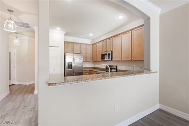 Kitchen featuring ornamental molding, light wood-type flooring, appliances with stainless steel finishes, light stone counters, and light brown cabinetry