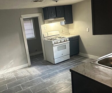 Kitchen with a textured ceiling, exhaust hood, white range with gas cooktop, and dark tile patterned flooring
