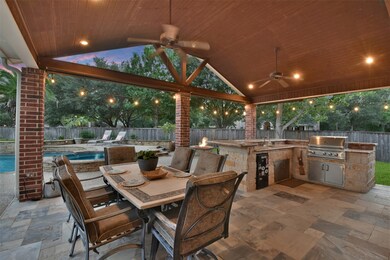 Fantastic outdoor living space with a large dining area and kitchen, surrounded by recessed lighting, ceiling fans, and travertine.